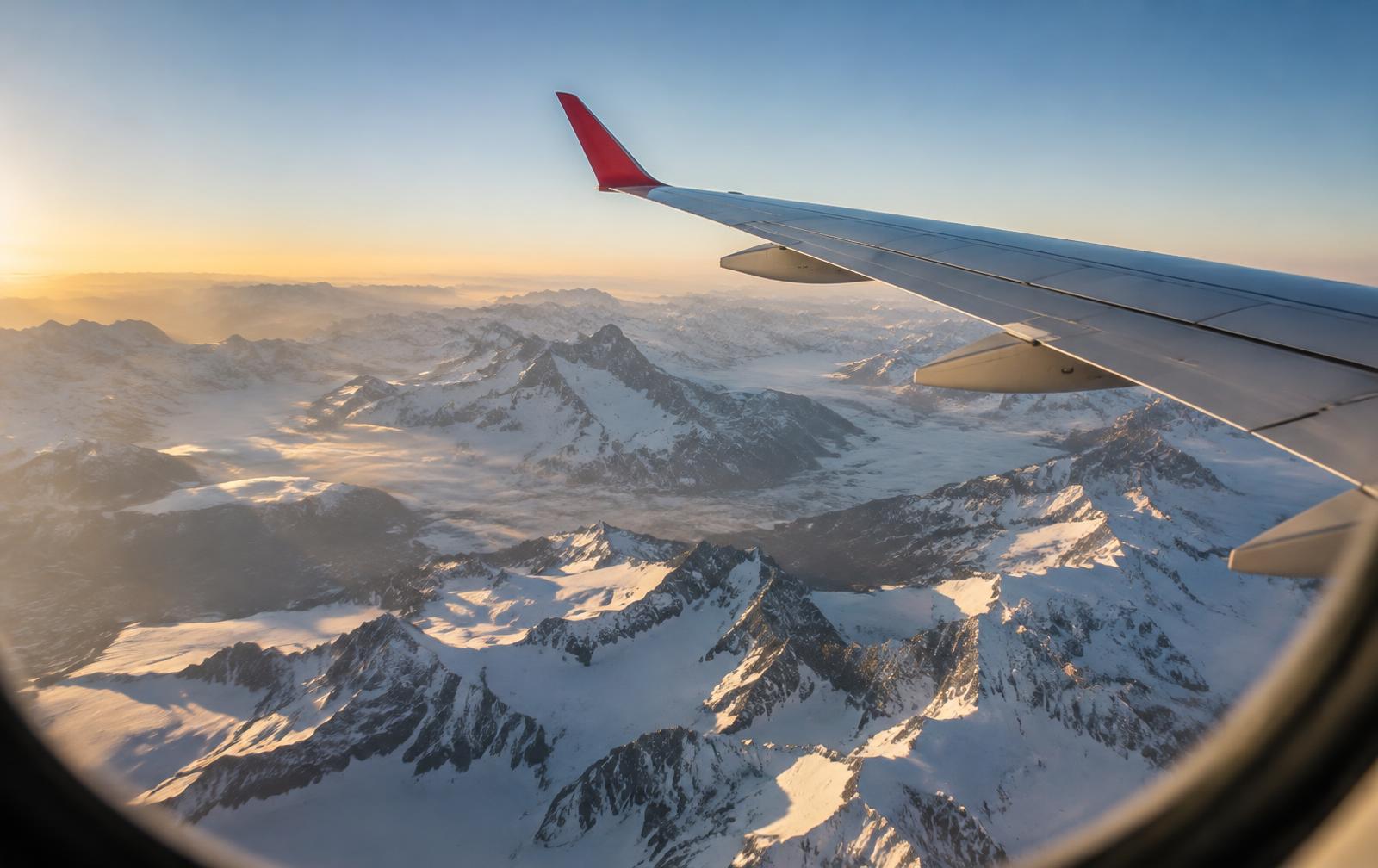 View from an airplane window over snow-covered Alps at sunrise