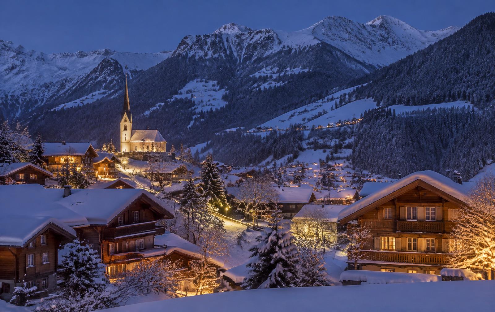 Snow-covered chalets with glowing windows in an alpine village at dusk